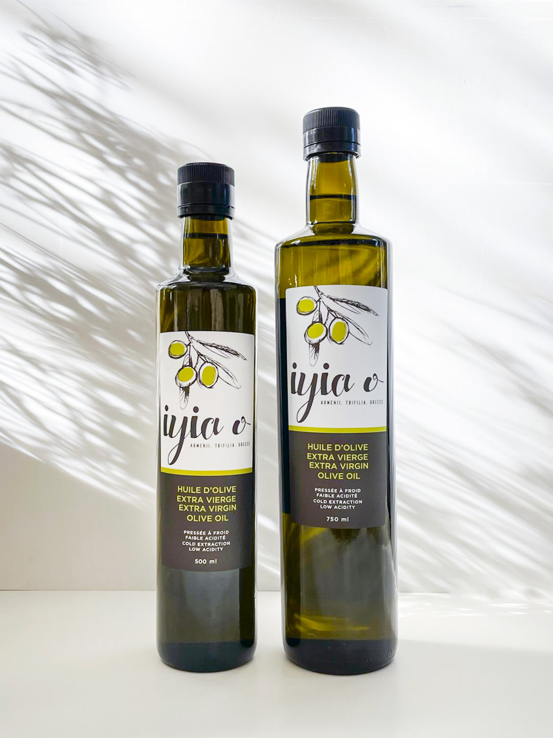 Iyia food group's Greek extra virgin olive oil in dark glass bottles: 500 ml and 750 ml on white surface side by side for size comparison.